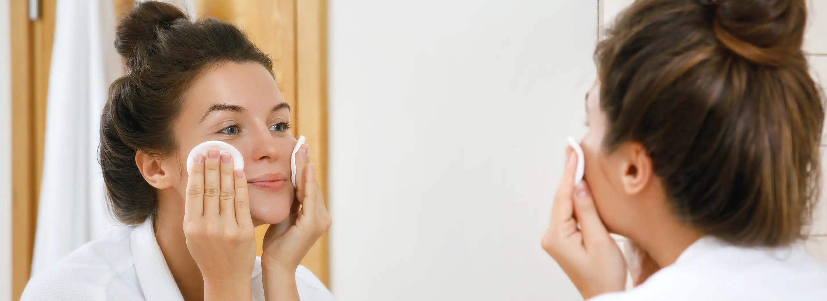 Pielęgnację sk&oacute;ry przed lustrem w łazience, ilustrująca problemy z pryszczami na policzkach i codzienną pielęgnację wspierającą mikrobiom sk&oacute;ry.