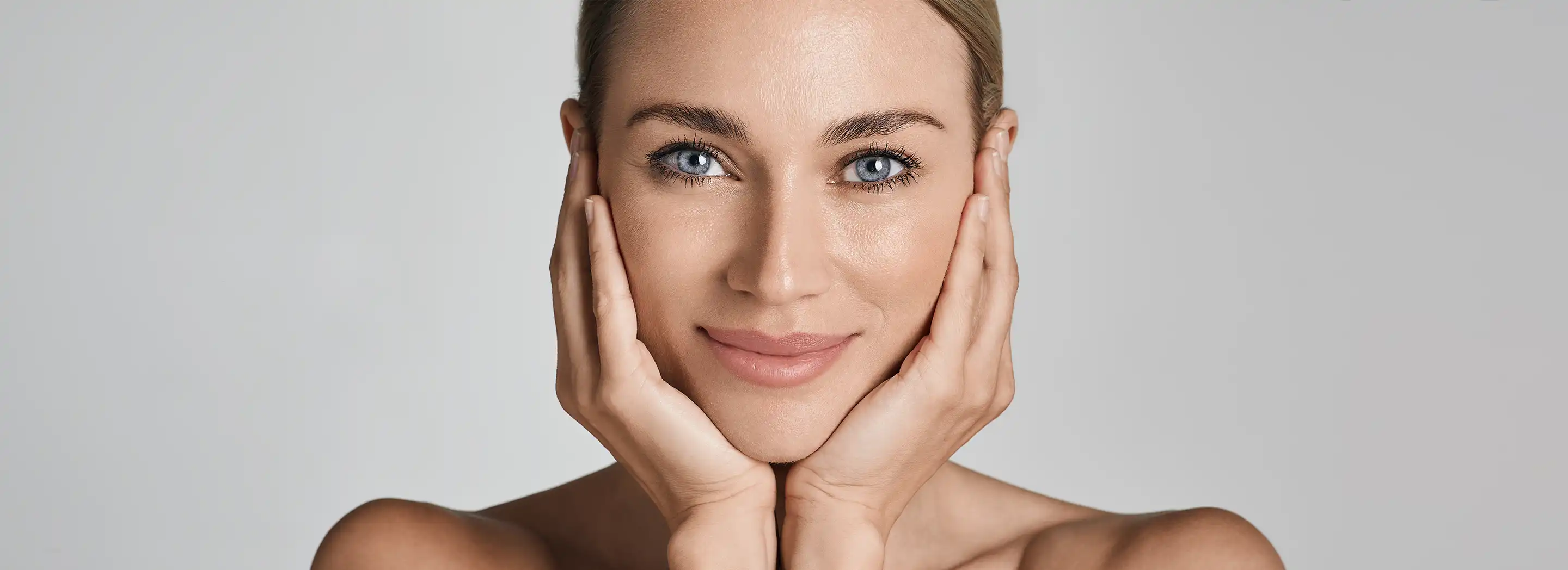 Osoba z odkrytymi ramionami dotykająca twarzy dłońmi, ilustrująca pielęgnację cery problematycznej i sezonowe zmiany w pielęgnacji sk&oacute;ry