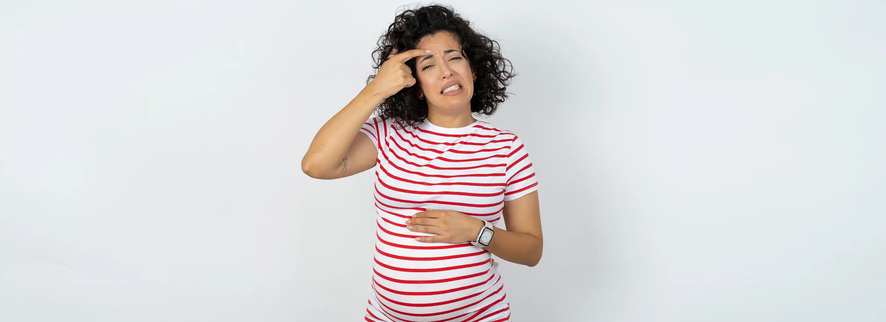 Osoba w ciąży dotykająca twarzy i brzucha na neutralnym tle, ilustrująca problem wyprysk&oacute;w na twarzy we wczesnej ciąży.