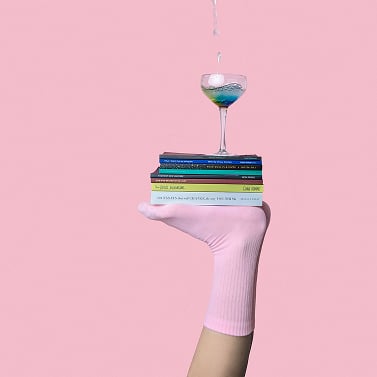 Stos książek z kieliszkiem na górze, na tle różowej ściany.