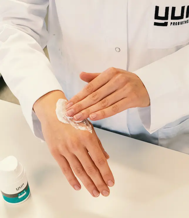 Osoba w białym fartuchu aplikuje krem Yun na dłoń, pokazując sposób użycia.